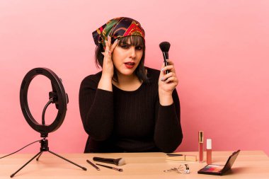 Makyaj sanatçısı genç bir kadın pembe arka planda özel bir makyaj dersi veriyor işaret parmağıyla yaptığı hayal kırıklığını gösteriyor..