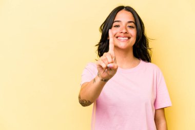 Sarı arka planda izole edilmiş genç İspanyol kadın bir numarayı parmağıyla gösteriyor..