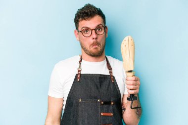 Kafkasyalı genç kunduracı, mavi arka planda izole edilmiş omuzlarını silkeliyor ve gözleri açık..