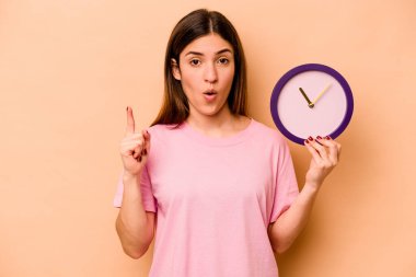 Elinde bej arka planda izole edilmiş bir saat tutan genç İspanyol kadının harika bir fikri var, yaratıcılık kavramı..