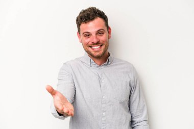 Beyaz arka planda izole edilmiş genç beyaz bir adam selamlama jesti olarak kameraya elini uzatıyor..