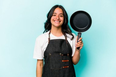 Young hispanic cooker woman holding frying pan isolated on blue background happy, smiling and cheerful.