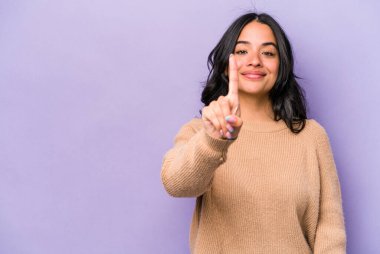 Mor arka planda izole edilmiş genç İspanyol kadın bir numarayı parmağıyla gösteriyor..