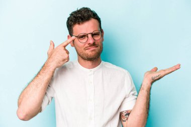 Mavi arka planda izole edilmiş genç beyaz adam işaret parmağıyla bir hayal kırıklığı jesti gösteriyor..