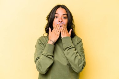 Sarı arka planda izole edilmiş genç İspanyol kadın elleriyle ağzını kapatırken şok oldu..