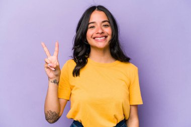 Mor arka planda izole edilmiş genç İspanyol kadın neşeli ve kaygısız parmakları olan bir barış sembolü gösteriyor..