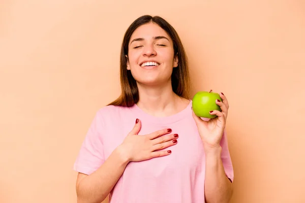 베이지 배경에서 고립된 사과를 지중해 여자가 가슴에 내밀고 소리로 웃는다 — 스톡 사진