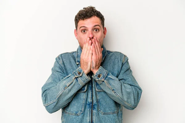 Beyaz arka planda izole edilmiş genç beyaz adam elleriyle ağzını kapatırken şok oldu..