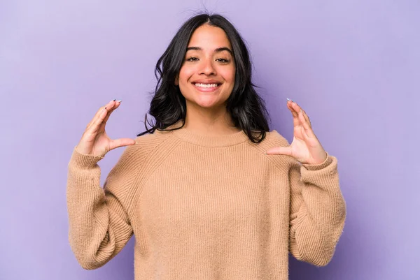 Mor arka planda izole edilmiş genç İspanyol kadın elinde avuç içi bir şeyle kameraya sunuyor..