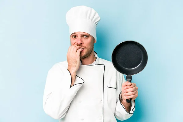 年轻的高加索厨师拿着用蓝色底咬指甲隔离的飞盘 紧张而焦虑 — 图库照片