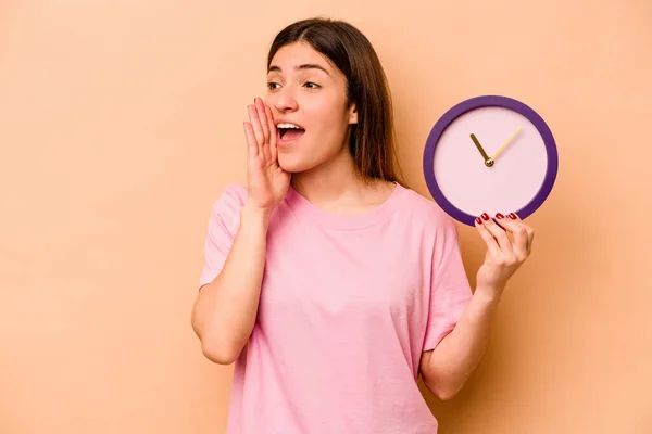 Mujer Hispana Joven Sosteniendo Reloj Aislado Sobre Fondo Beige Gritando —  Fotos de Stock