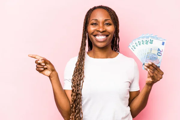 Mladá Afroameričanka Drží Bankovky Izolované Růžovém Pozadí Usmívá Ukazuje Stranou — Stock fotografie