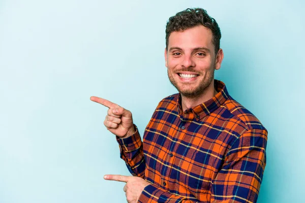 Kafkasyalı genç adam mavi arka planda izole edilmiş. İşaret parmağıyla işaret ettiği için heyecanlı..