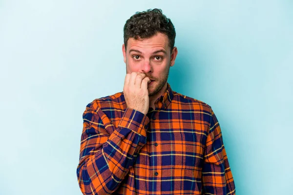 Mavi arka planda izole edilmiş, tırnak yiyen, gergin ve endişeli genç bir beyaz adam..