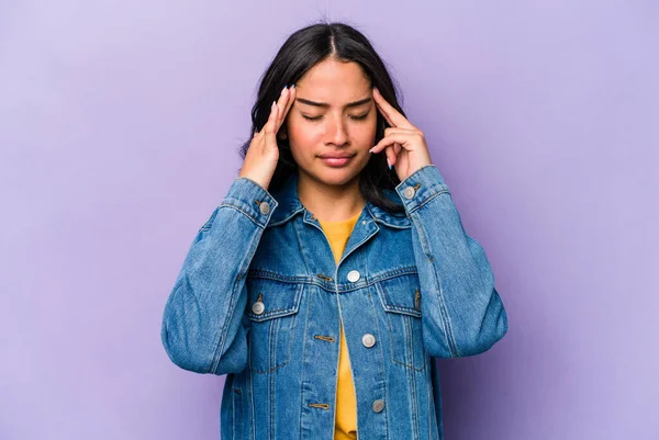 Mor arka planda izole edilmiş genç İspanyol kadın şakaklara dokunuyor ve baş ağrısı çekiyor..