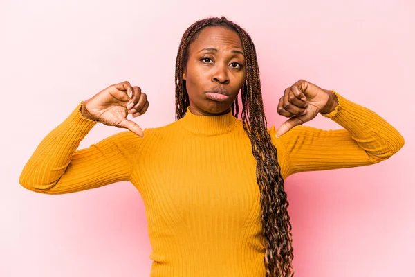 Genç Afro-Amerikalı kadın pembe arka planda izole edilmiş, hoşlanmadığı bir jest gösteriyor, başparmakları aşağıda. Anlaşmazlık konsepti.