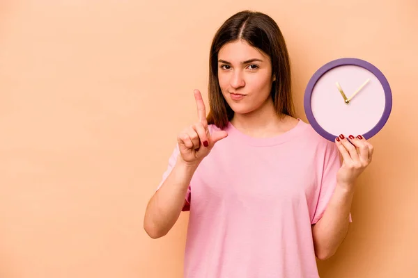 Mujer Hispana Joven Sosteniendo Reloj Aislado Sobre Fondo Beige Mostrando — Foto de Stock