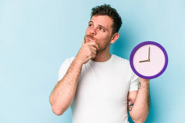 Jonge Blanke Man Houdt Een Klok Geïsoleerd Blauwe Achtergrond Kijken — Stockfoto