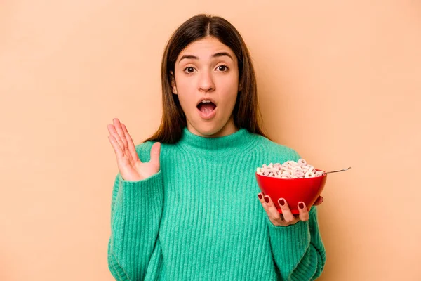 Jonge Spaanse Vrouw Eten Granen Geïsoleerd Beige Achtergrond Verrast Geschokt — Stockfoto