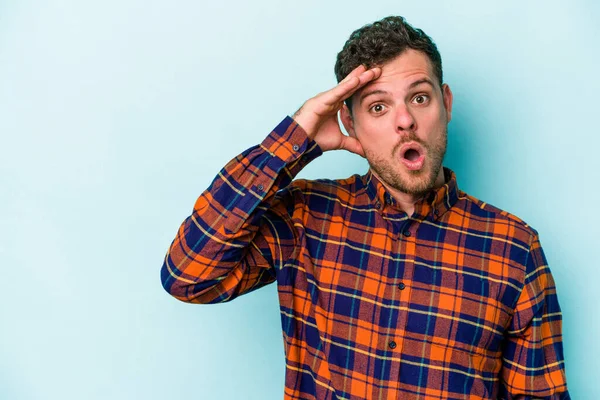 Mavi arka planda izole edilmiş genç beyaz adam yüksek sesle bağırıyor, gözleri açık ve elleri gergin tutuyor..