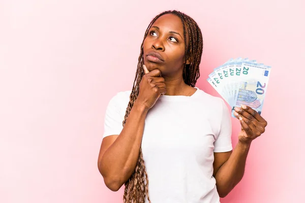 Молодая Афроамериканка Банкнотами Розовом Фоне Смотрит Сторону Сомнительным Скептическим Выражением — стоковое фото