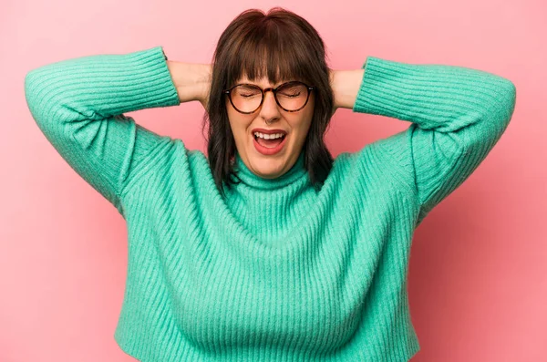 Pembe arka planda izole edilmiş genç, beyaz bir kadın. Kulakları kulaklarıyla kapatıyor. Çok fazla ses duymamaya çalışıyor..