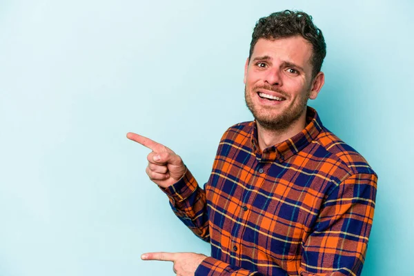 Mavi arka planda izole edilmiş genç beyaz adam işaret parmağıyla fotokopi alanını işaret ederek şok oldu..