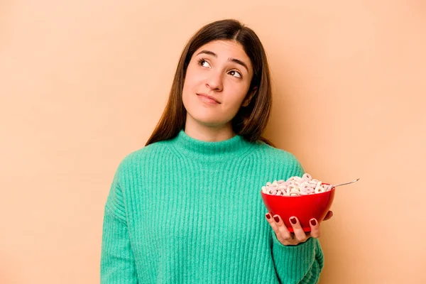 Jovem Hispânica Comendo Cereais Isolados Fundo Bege Sonhando Alcançar Objetivos — Fotografia de Stock