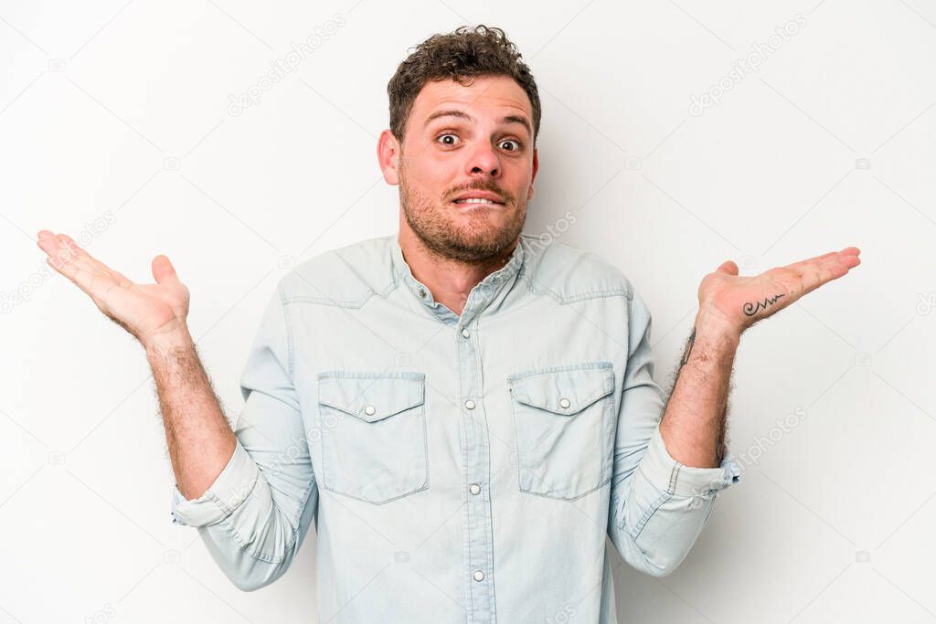 Young caucasian man isolated on white background confused and doubtful shrugging shoulders to hold a copy space.