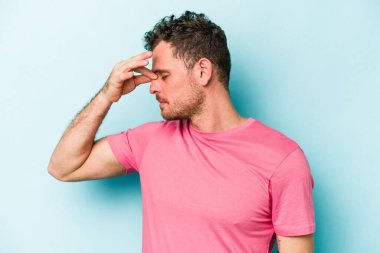 Kafkasyalı genç bir adam mavi arka planda izole edilmiş, başı ağrıyor, yüzüne dokunuyor..