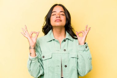 Sarı arka planda izole edilmiş genç İspanyol kadın sıkı çalışma gününden sonra rahatlıyor, yoga yapıyor..