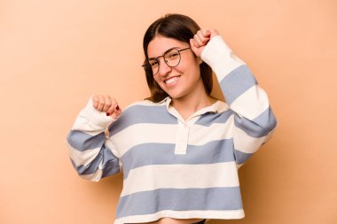 Latin kökenli genç bir kadın bej arka planda izole edilmiş özel bir günü kutluyor, atlıyor ve enerjiyle kollarını kaldırıyor..