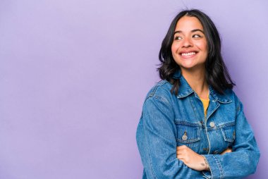 Mor arka planda soyutlanmış genç İspanyol kadın kollarını kavuşturarak gülümsüyor..