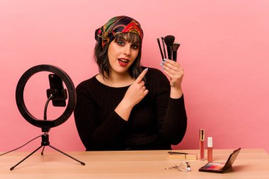 Makyaj sanatçısı genç bir kadın pembe arka planda özel bir makyaj dersi veriyor.