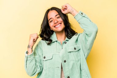 Sarı arka planda izole edilmiş genç İspanyol kadın özel bir günü kutluyor, atlıyor ve enerjiyle kollarını kaldırıyor..