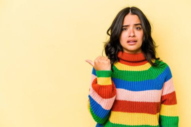 Sarı arka planda izole edilmiş genç İspanyol kadın işaret parmağıyla fotokopi alanını işaret ederek şok oldu..