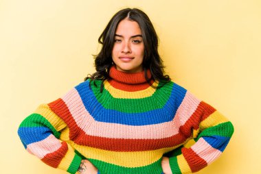 Sarı arka planda izole edilmiş, hoşnutsuzca kaşlarını çatan, kollarını kavuşturan genç İspanyol kadın..