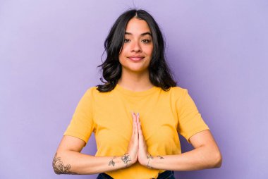 Genç İspanyol kadın mor arka planda izole edilmiş dua ediyor, bağlılık gösteriyor, dindar biri ilahi ilham arıyor..