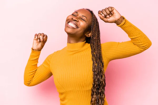 Pembe arka planda izole edilmiş genç Afrikalı Amerikalı kadın özel bir günü kutluyor, atlıyor ve enerjiyle kollarını kaldırıyor..