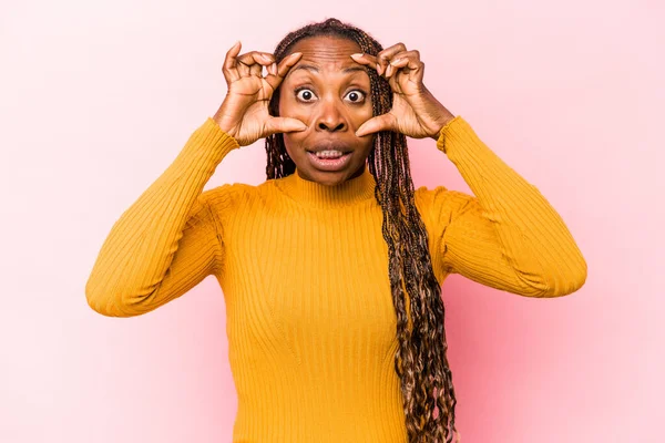 Genç Afrikalı Amerikalı kadın pembe arka planda izole edilmiş bir şekilde gözlerini açık tutarak başarı fırsatı arıyor..