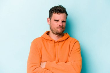 Mavi arka planda izole edilmiş genç beyaz adam alaycı bir ifadeyle kameraya bakarken mutsuz oluyor..