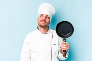 Kafkasyalı genç aşçı elinde uçan tavayla mavi arka planda tek başına hedeflere ve amaçlara ulaşmayı hayal ediyor.