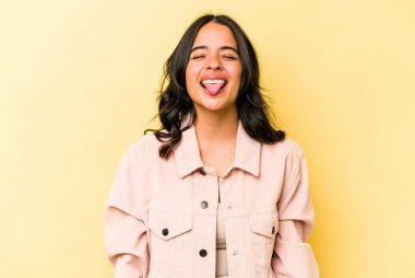 Sarı arka planda izole edilmiş genç bir İspanyol kadın. Komik ve dost canlısı bir dil uzatıyor..