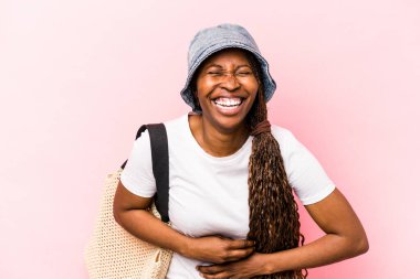 Genç Afrikalı Amerikalı bir kadın pembe arka planda izole bir şekilde kumsala gidiyor. Gülüyor ve eğleniyor..