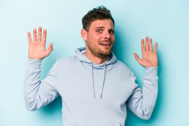 Mavi arka planda izole genç beyaz adam yakın bir tehlike nedeniyle şoka uğruyor