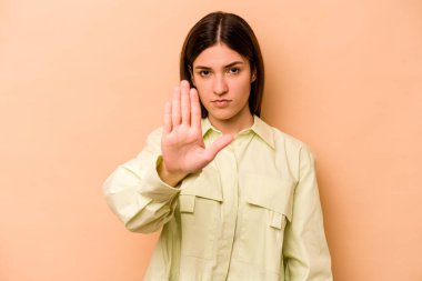 Latin kökenli genç bir kadın, bej arka planda izole edilmiş, elini uzatmış, dur işareti göstererek seni engelliyor..