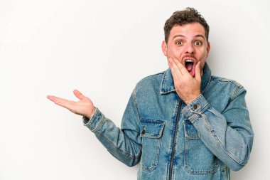 Beyaz arka planda izole edilmiş genç beyaz bir adam bir avuç içinde fotokopi alanı tutuyor, el üstünde tutuyor. Şaşırmış ve mutlu..