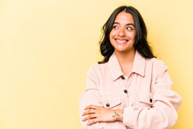 Sarı arka planda izole edilmiş genç İspanyol kadın kollarını kavuşturarak gülümsüyor..