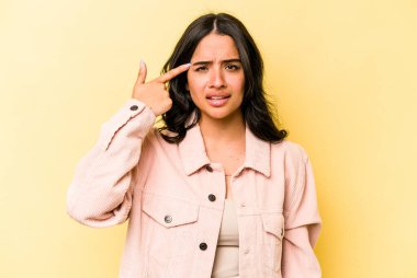 Sarı arka planda izole edilmiş genç İspanyol kadın işaret parmağıyla bir hayal kırıklığı gösteriyor..