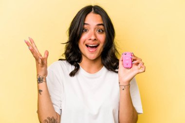 Pembe arka planda izole edilmiş anahtar taşıyan genç İspanyol kadın hoş bir sürpriz alıyor, heyecanlı ve el kaldırıyor..